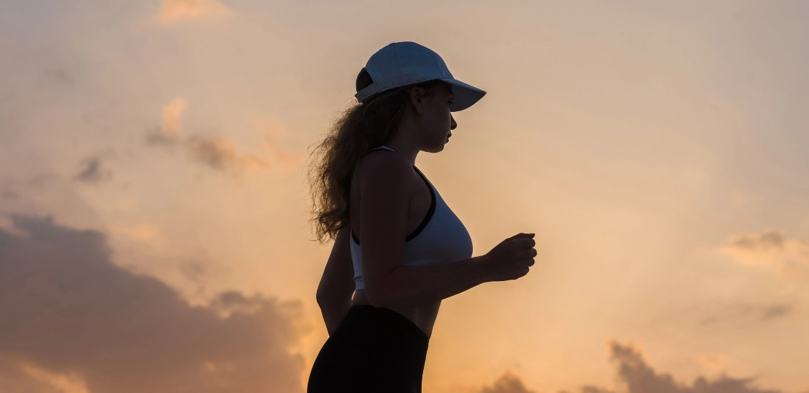 kobieta biegnąca na tle zachodzącego słońca